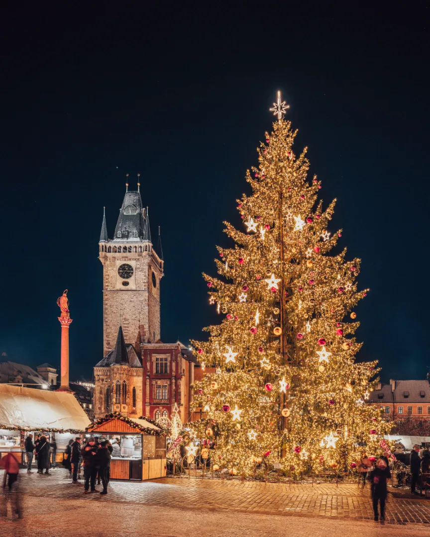 A decorated Christmas tree and market stalls in Prague’s Old Town Square, with a Gothic tower behind.